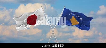 Flaggen von Japan und Kosovo winken im Wind auf Fahnenmasten gegen den Himmel mit Wolken am sonnigen Tag. Ein Symbol für die Beziehung, den Dialog zwischen zwei Ländern Stockfoto