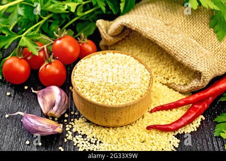 Roher Couscous in einer Schüssel und ein Sack mit Sackleinen, Tomaten, Paprika, Kräutern und Knoblauch auf Holzbrett Hintergrund Stockfoto