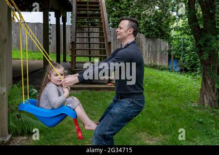 Lynwood, Washington, USA. Mann zieht an der Schaukel seiner 4-jährigen Tochter. (MR) Stockfoto