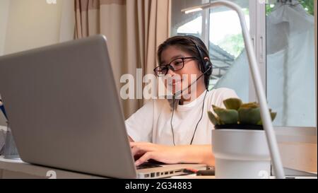 Asiatische Mädchen in Kopfhörer sitzen am Schreibtisch Studie online auf Laptop. Kinder tragen Headset-Handschrift beim Lernen im Notebook mit Hilfe von Internet-Lektionen über Quarantäne. G Stockfoto
