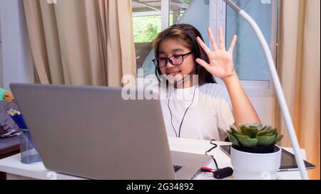 Asiatische Mädchen in Kopfhörer sitzen am Schreibtisch Studie online auf Laptop. Kinder tragen Headset-Handschrift beim Lernen im Notebook mit Hilfe von Internet-Lektionen über Quarantäne. G Stockfoto