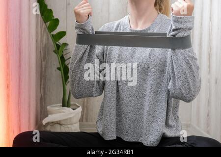 Handarm Übungen mit Gummiband Junge tausendjährige blonde Frau macht Yoga-Übung Stretching Fitness auf Balkon zu Hause. Achtsamkeitsmeditation. Relax Breathe easy Pose Fitnessstudio gesundes Lifestyle-Konzept. Selbstisolierung ist von Vorteil Stockfoto