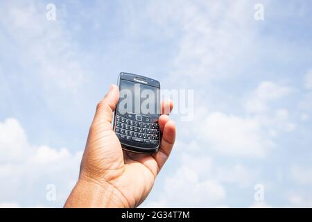 Eine Hand hält ein veraltetes Blackberry-Smartphone in den Himmel. Stockfoto