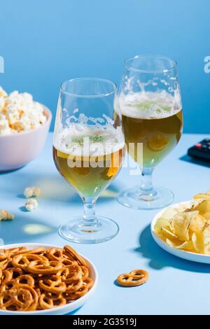 Eine Auswahl ungesunder Snacks, wie Chips, Popcorn, Brezeln, in Schüsseln und Gläsern mit leichtem Bier. Stockfoto