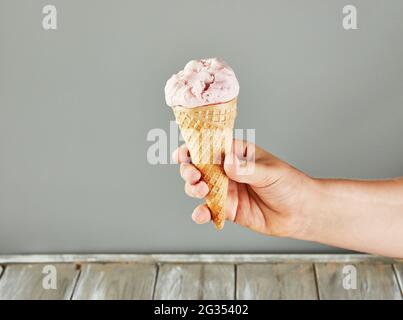 Handgehaltener Waffelkegel mit Eiscreme auf grauem Hintergrund Stockfoto
