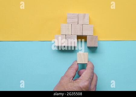 Hand des Mannes, der ein Stück Holzblock einführt, um eine Pyramidenform von Holzblöcken zu vervollständigen. Draufsicht. Stockfoto