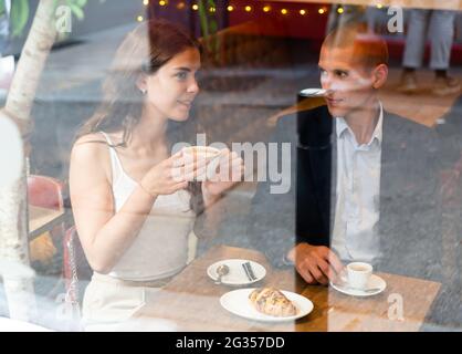 Ein elegantes Paar redet und trinkt Kaffee am Tisch in einem Café. Blick von der Straße Stockfoto