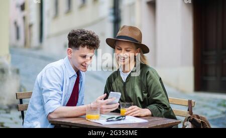 Junge Paare, die im Urlaub in der Stadt ein Smartphone benutzen, sitzen im Café im Freien. Stockfoto