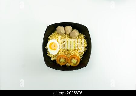 Warme Nudeln mit Eiern und frischen Tomaten mit Fleischbällchen auf einer schwarzen Schüssel serviert und auf einer weißen Schüssel auf weißem Hintergrund eingelegt Stockfoto