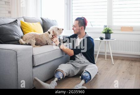 Porträt eines behinderten jungen Mannes, der zuhause mit dem Hund spielt, Beinprothetik. Stockfoto