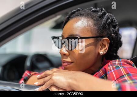 Nahaufnahme einer afroamerikanischen Frau, die sich auf das Fenster ihres Autos stützt: Selektiver Fokus und Nahaufnahme. Stockfoto