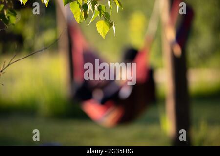 Eine entspannende Frau in einer Hängematte an einem warmen, englischen Sommerabend, weicher Fokus, eingerahmt von Blättern Stockfoto