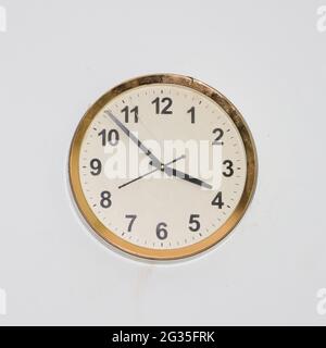 Große, runde Uhr mit einem alten, einfachen Design und einem goldenen Rahmen, der an einer weißen Wand hängt und die genaue Zeit anzeigt Stockfoto