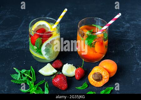 Erfrischende Sommergetränke mit Zitronen-, Erdbeer- und Aprikosenscheiben in Gläsern auf schwarzem Hintergrund. Stockfoto