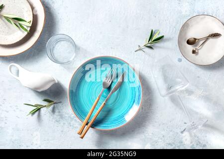 Trendiges Geschirr mit einem blauen Teller, von oben geschossen. Essgeschirr-Set zum Abendessen, mit Olivenzweigen zur Einrichtung, mediterranes Food-Konzept. Elegante Gerichte Stockfoto