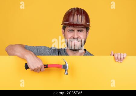 Glücklicher reifer Mann Arbeiter im Helm hinter gelbem Papier für Kopierraum halten Hammer, glücklicher Arbeiter Tag Stockfoto
