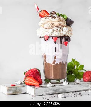 Schokolade und Erdbeermilchshake mit Eis und Schlagsahne, Mini-Baiser, Schokolade, Erdbeere und Minze in einem Glas serviert. Selektiver Fokus. Stockfoto