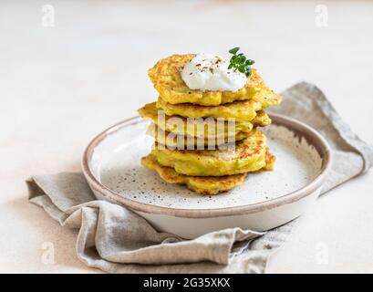 Stapel von Gemüsefrittern oder Pfannkuchen mit Joghurt oder saurem Dressing und Kräutern. Kohl oder Zucchini-Krapfen auf Keramikplatte. Gesunder Vegetari Stockfoto