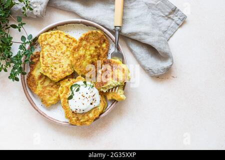 Gemüsefritter oder Pfannkuchen mit Joghurt oder saurem Dressing und Kräutern. Kohl oder Zucchini-Krapfen auf Keramikplatte. Gesundes vegetarisches Essen. Stockfoto