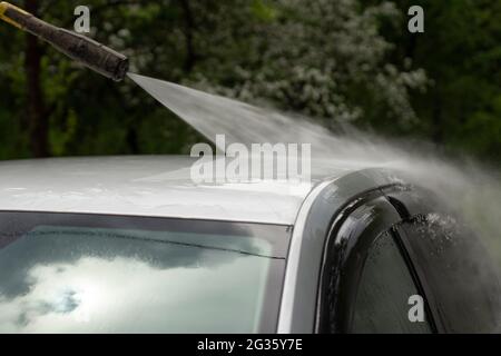 Autowäsche. Das Auto wird unter dem Druck eines Wasserstrahls gewaschen. Mit einem Wasserspray Schmutz von der Fahrzeugoberfläche abwaschen. Stockfoto