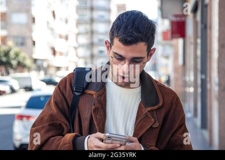 Überraschender Mann, der auf der Straße auf das Mobiltelefon schaute Stockfoto
