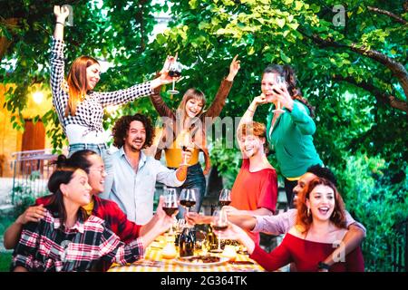Freunde, die Spaß haben, Rotwein im Freien auf der Gartenparty zu toasten - glückliche Leute, die in der Nacht im Bauernweingut zusammen essen und trinken Stockfoto