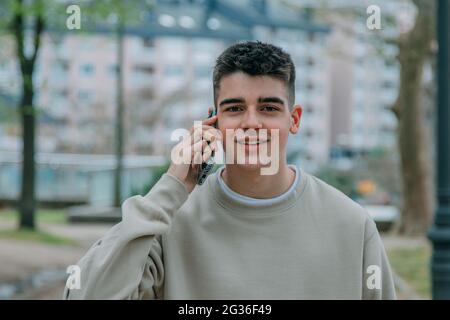 Männlicher Teenager, der auf der Straße mit dem Handy telefoniert Stockfoto