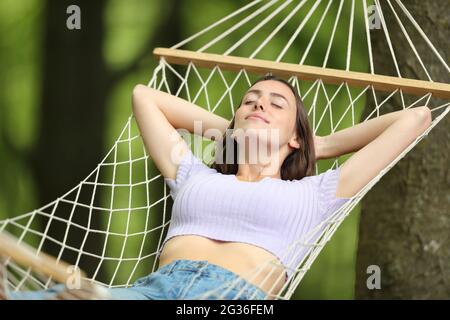 Entspannte Frau im Sommerurlaub, die sich auf einer Seilhängematte in einem Wald ausruht Stockfoto