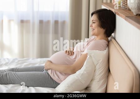 Seitenansicht lächelnde, schwanger Frau, die sich auf dem Bett entspannt und den Bauch berührt Stockfoto