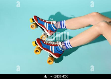 Junge Frau mit dünnen, dünnen Beinen, die bunte Rollschuhe mit gelben Rädern trägt und einen Blick auf ihre Beine, die sich von rechts über einen blauen Rückengr erstreckt Stockfoto