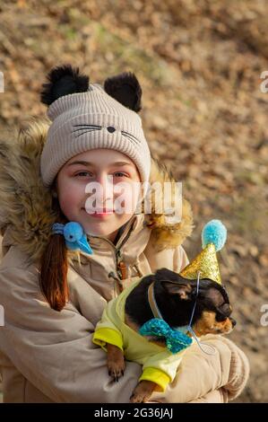 Außenportrait eines 10- 11-jährigen Mädchens in warmer beigefarbener Jacke mit einem chihuahua Hund. Geburtstag Stockfoto