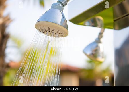 Erfrischender Duschkopf im Freien, der Wasser spritzt, um vor dem Schwimmen im Pool oder im Meer im Resort zu duschen. Stockfoto