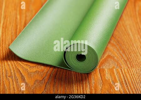 Eine grüne Yogamatte ist in einer Rolle auf dem Holzboden angelegt. Ein gesunder Lebensstil in Isolation. Stockfoto