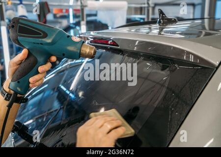 Der professionelle Detailer wärmt die Tönfolie mit einem Industrietrockner auf, um Tönungen auf Autoglas aus nächster Nähe zu auftragen. Stockfoto