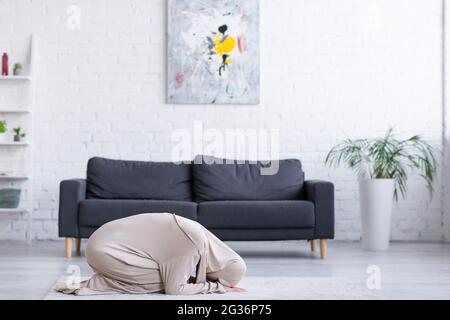 Junge muslimische Frau, die im Wohnzimmer auf dem Boden betet Stockfoto