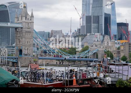 Da sich das Finanzviertel der Hauptstadt (die Square Mile) in der Ferne befindet, sitzen verschlossene Fahrräder auf einem Boot an der Tower Bridge Moorings werden am 11. Juni 2021 an der Themse in London, England, zusammengefasst. Tower Bridge Moorings ist der einzige schwimmende Garten der Hauptstadt - eine nachhaltige Lebensweise für eine Gemeinschaft von mehr als hundert Erwachsenen und Kindern und ein Schutz für Wildtiere auf dem Fluss. Tower Bridge Moorings ist der einzige schwimmende Garten der Hauptstadt - eine nachhaltige Lebensweise für eine Gemeinschaft von mehr als hundert Erwachsenen und Kindern und ein Schutz für Wildtiere auf dem Fluss. Stockfoto