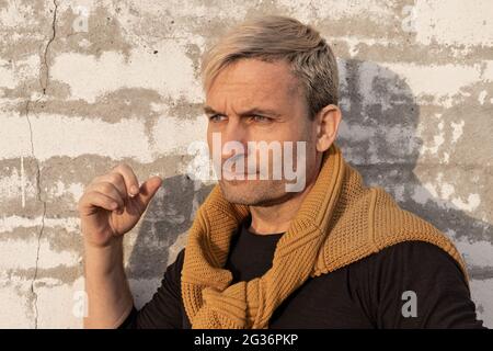 Nachdenkliche stilvolle charmante blonde mittleren Alters Mann des Modells Auftritt vor einer weißen Backsteinmauer. Hübsch reifen männlichen Modell in Casual Mode kleiden Stockfoto