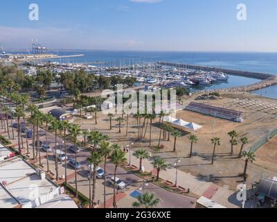 Top Luftbild mit Blick auf Finikoudes Promenade mit Palmen, Yachten im Hafen und Volleyballplatz am Mittelmeer an einem sonnigen Tag. Stockfoto