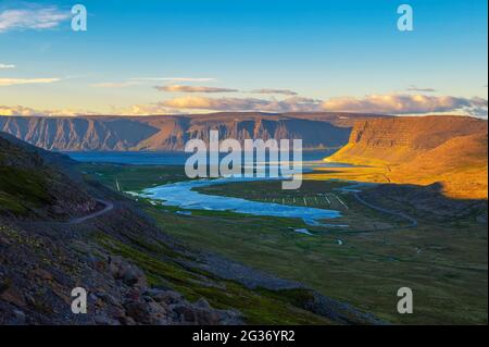 Isländische Landschaft mit Fjord und Schotterstraße bei Sonnenuntergang in Westfjorden, Island Stockfoto