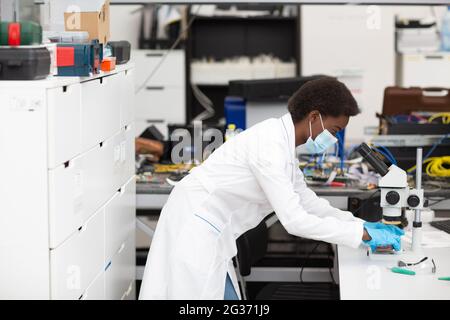 Wissenschaftlerin afroamerikanische Frau, die im Labor mit Instrumenten und Mikroskop arbeitet. Farbe Frau in Tech. Stockfoto