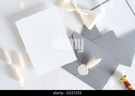 Elegante Hochzeit Schreibwaren Mockup Szene. Unbeschriftete Grußkarte, grauer Umschlag mit Wachsstempel, getrocknete Blumen auf pastellweißem Hintergrund. Flaches Lay, t Stockfoto