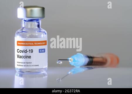 Fläschchen mit COVID-19-Impfstoff und Spritze mit Impfstofftropfen, die in der Nähe an der Nadelspitze hängen. Impfungen, Covid-19, Pharmaindustrie und Stockfoto