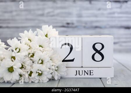 Kalenderblöcke aus weißem Holz mit dem Datum 28. Juni und weißen Gänseblümchen. Selektiver Fokus mit unscharfem Hintergrund. Stockfoto