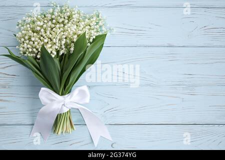 Blumenstrauß aus Lilien des Tales mit einem weißen Band auf blauem Hintergrund. Postkartenkonzept. Kopieren Sie die Spase. Stockfoto
