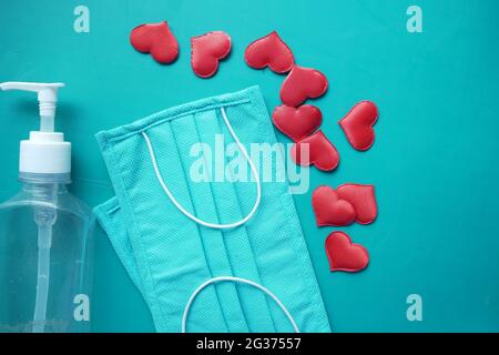 Chirurgische Masken mit Herzform und Handdesinfektionsmittel auf Farbe Hintergrund Stockfoto