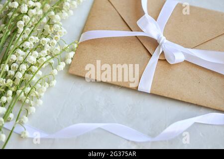 Bouquet von Lilien des Tals, Handwerk Umschlag mit einer Schleife auf blauem Hintergrund. Draufsicht. Stockfoto