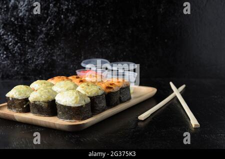 Ein Satz Reisrollen mit Meeresfrüchten, eingewickelt in dünne getrocknete Seegrasblätter auf einer Holzplatte mit Ingwer und Wasabi auf schwarzem Holzgrund. Selektiv Stockfoto