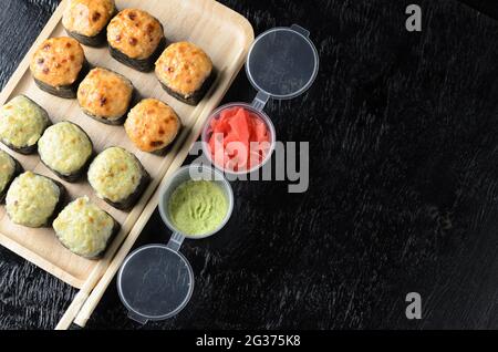 Ein Satz Reisrollen mit Meeresfrüchten, eingewickelt in dünne getrocknete Seegrasblätter auf einer Holzplatte mit Ingwer und Wasabi auf schwarzem Holzgrund. Selektiv Stockfoto