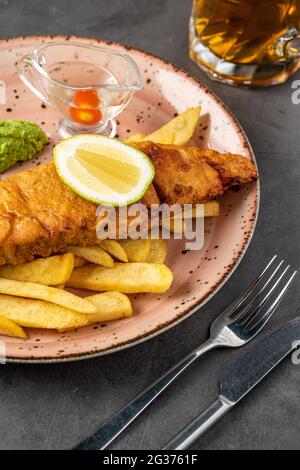 Traditionelle britische Fish and Chips mit pürierten Erbsen, Erbsensauce und kaltem Bier. Stockfoto