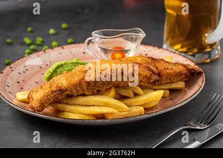 Traditionelle britische Fish and Chips mit pürierten Erbsen, Erbsensauce und kaltem Bier. Stockfoto